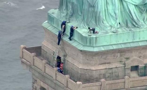 Una manifestante se encarama a la Estatua de la Libertad para confrontar las política de Trump